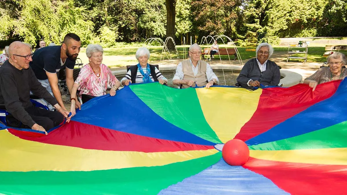 Pfleger und Bewohner von PFLEGEN & WOHNEN HAMBURG Farmsen spielen mit einem bunten Schwungtuch und einem Ball.