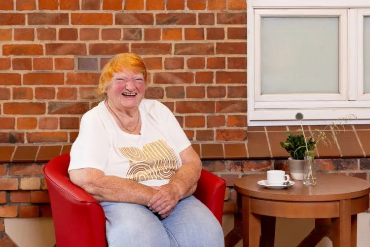 Karen Mehani, Bewohnerin bei PFLEGEN & WOHNEN HAMBURG am Standort Farmsen, am Tisch mit einer Tasse Kaffee.