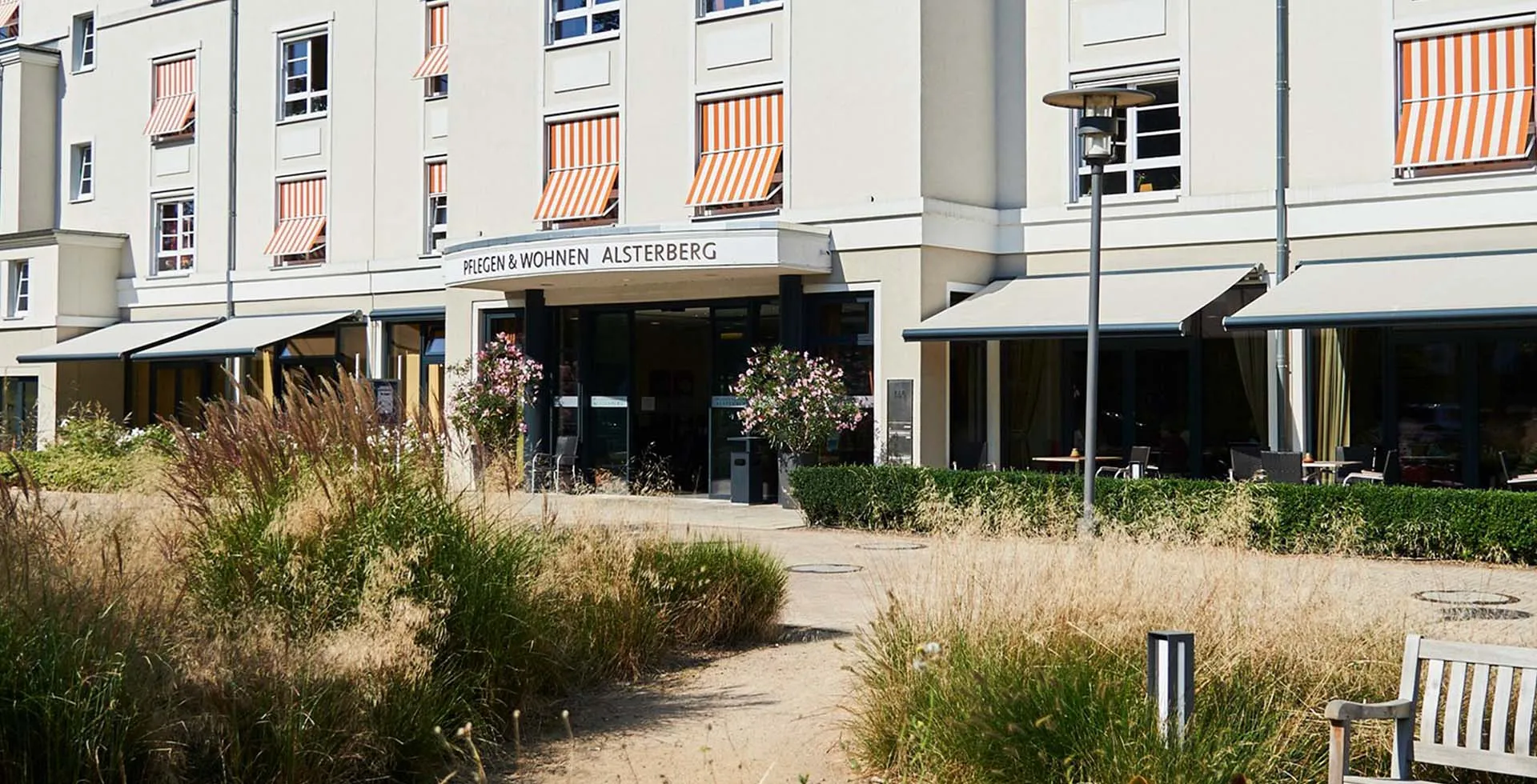 Haupteingang von PFLEGEN & WOHNEN HAMBURG am Standort Alsterberg mit gepflegtem Garten, Ruhebänken und Eingangsbereich.