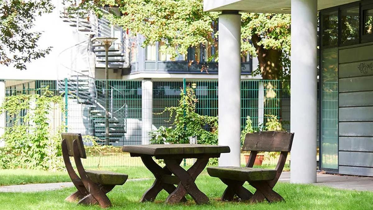 Der Außenbereich mit Sitzmöglichkeiten und Tisch aus Holz bei PFLEGEN & WOHNEN HAMBURG in Uhlenhorst.