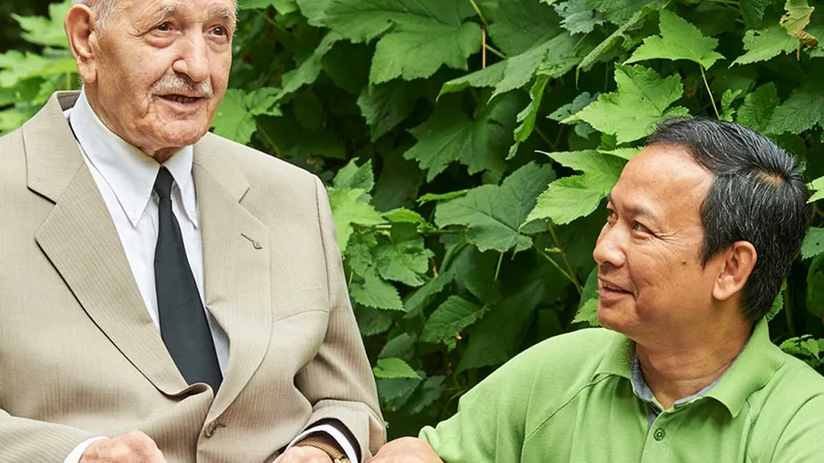 Pfleger kniet vor einem Bewohner von PFLEGEN & WOHNEN HAMBURG in Horn und unterhält sich mit ihm.