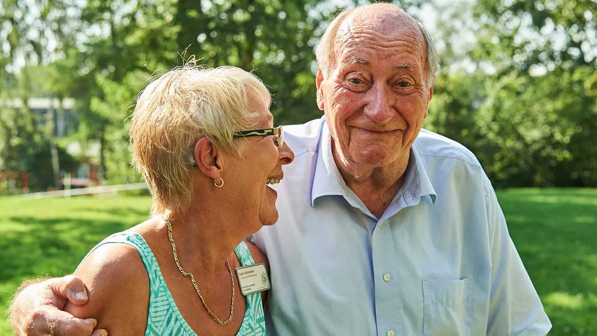 Bewohner des PFLEGEN & WOHNEN HAMBURG-Standorts Alsterberg nimmt lachende Mitarbeiterin in den Arm.