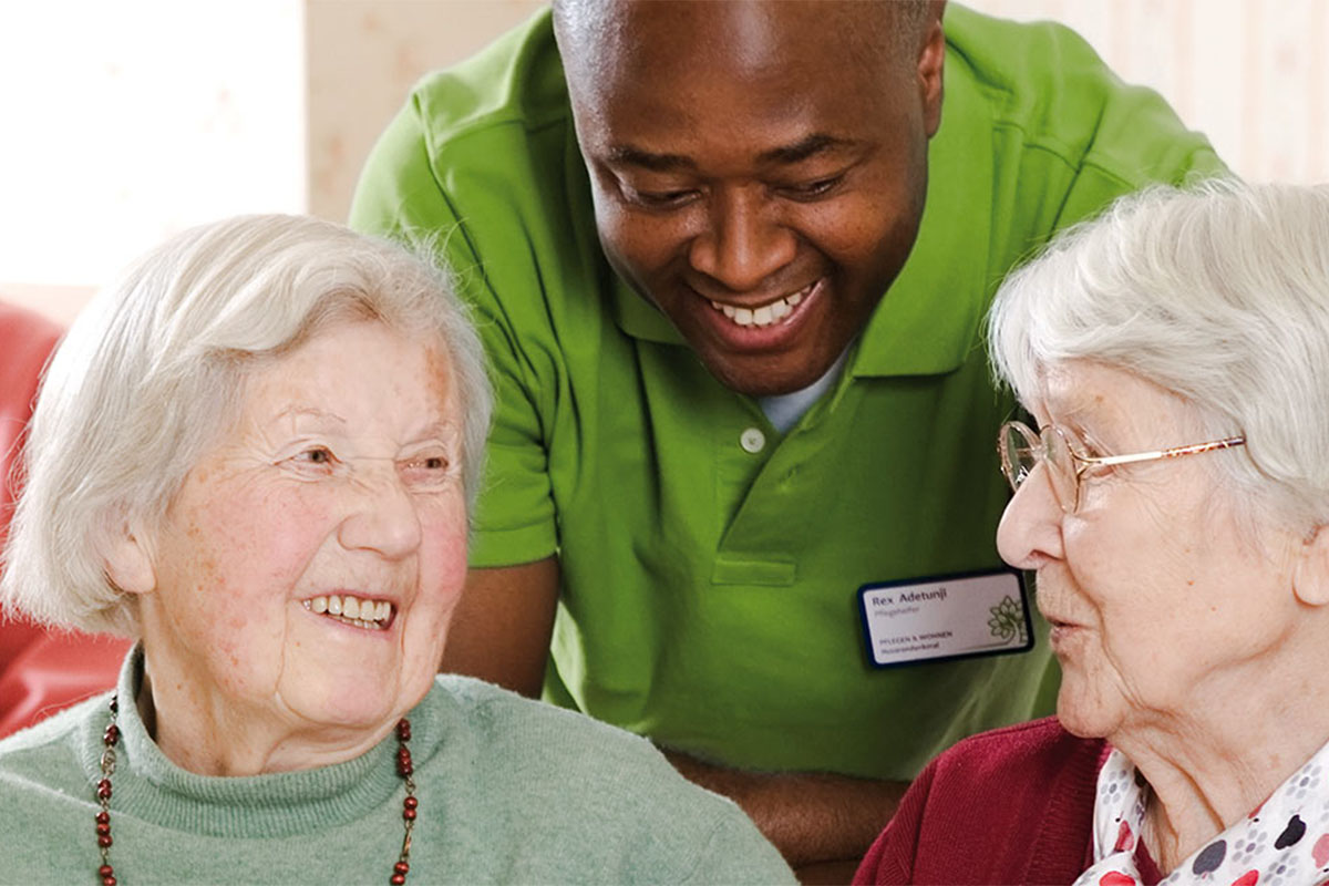 Zwei Senior:innen führen ein angeregtes Gespräch, bei dem auch die Pflege aufmerksam teilnimmt.