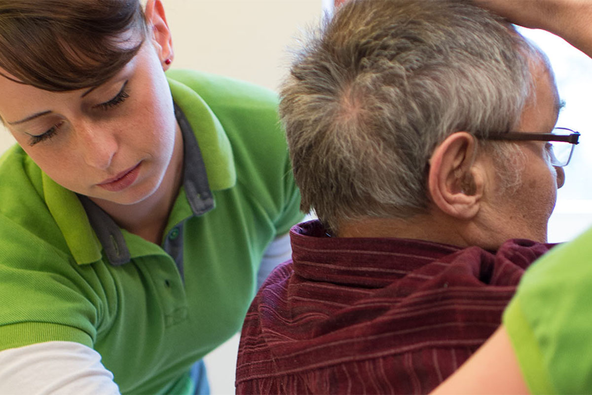 Zwei Pflegekräfte von PFLEGEN & WOHNEN HAMBURG unterstützen einen Bewohner beim Ankleiden.