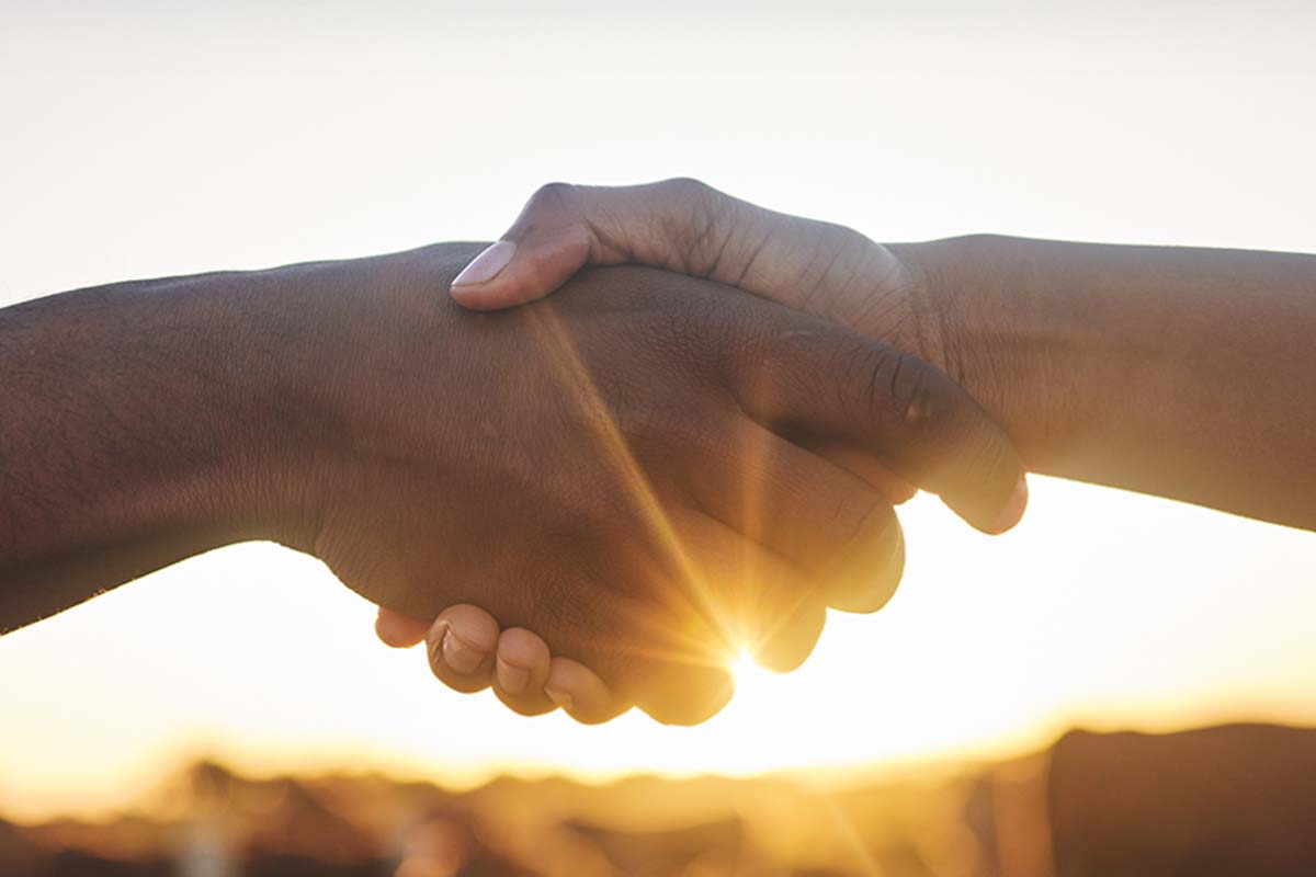 Ein Handschlag vor der Kulisse eines warmen Sonnenuntergangs – ein Zeichen von Verbindung und Vertrauen.