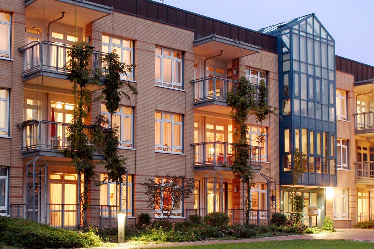 Außenansicht von PFLEGEN & WOHNEN HAMBURG Moosberg, mit grünem, modernen Eingangsbereich und Balkonen für Seniorenpflege.